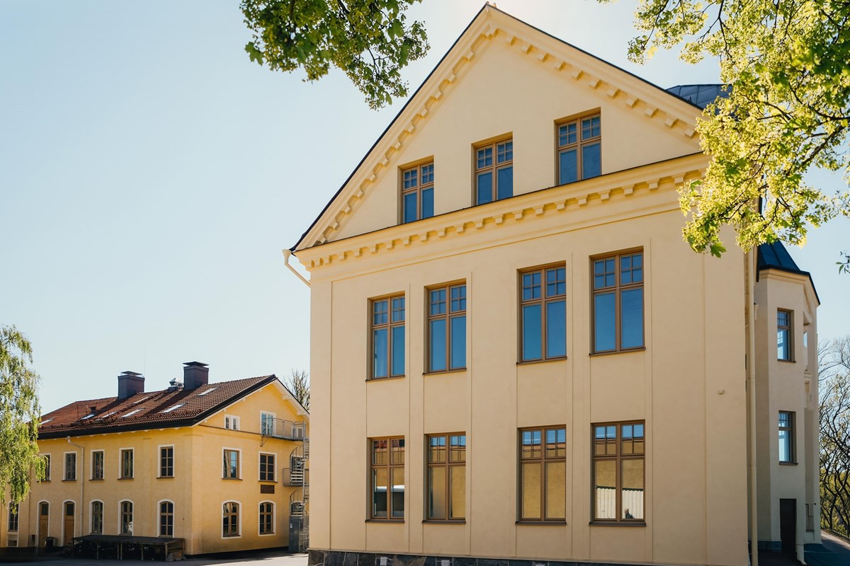 Byggnadens gavel med höga fönster och intilliggande fastighet.